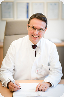 Arzt mit Brille sitzt am Schreibtisch und schreibt, Radiologie Unimedizin Rostock