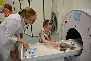 kleines Mädchen schiebt mit Studentin in Kittel Kuscheltier in Spielzeug-MRT-Gerät, radiologie rostock