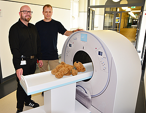 zwei Männer in schwarz stehen vor Spielzeug-MRT mit Kuscheltier, radiologie rostock